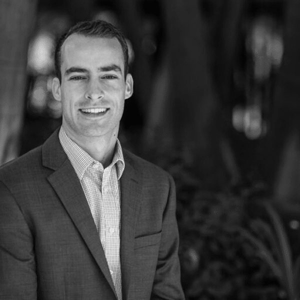 Black and white portrait of a smiling man in a suit outdoors.