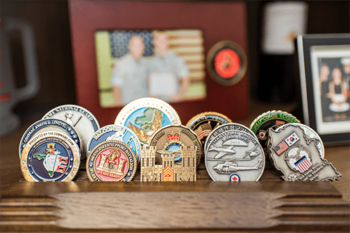 Military challenge coins on wooden display rack.