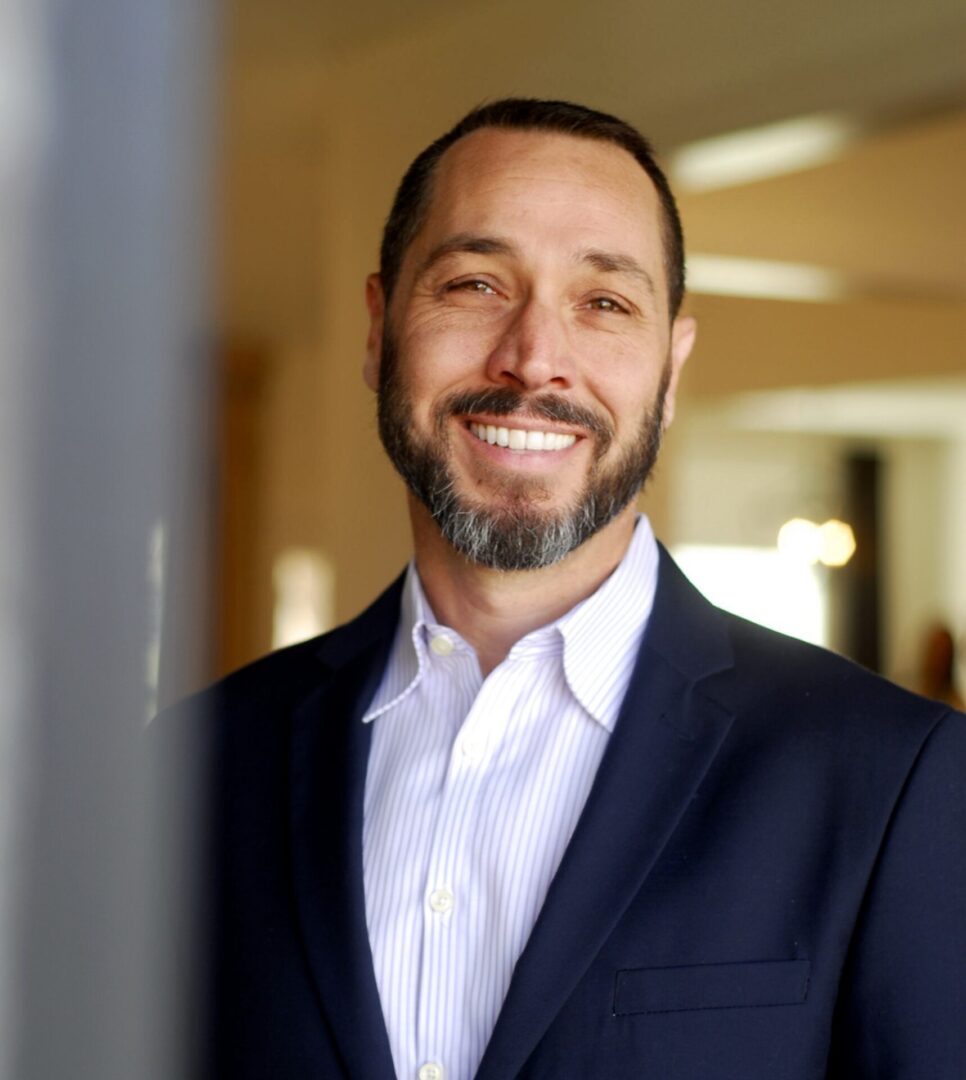 Smiling man in a suit posing indoors with soft lighting.